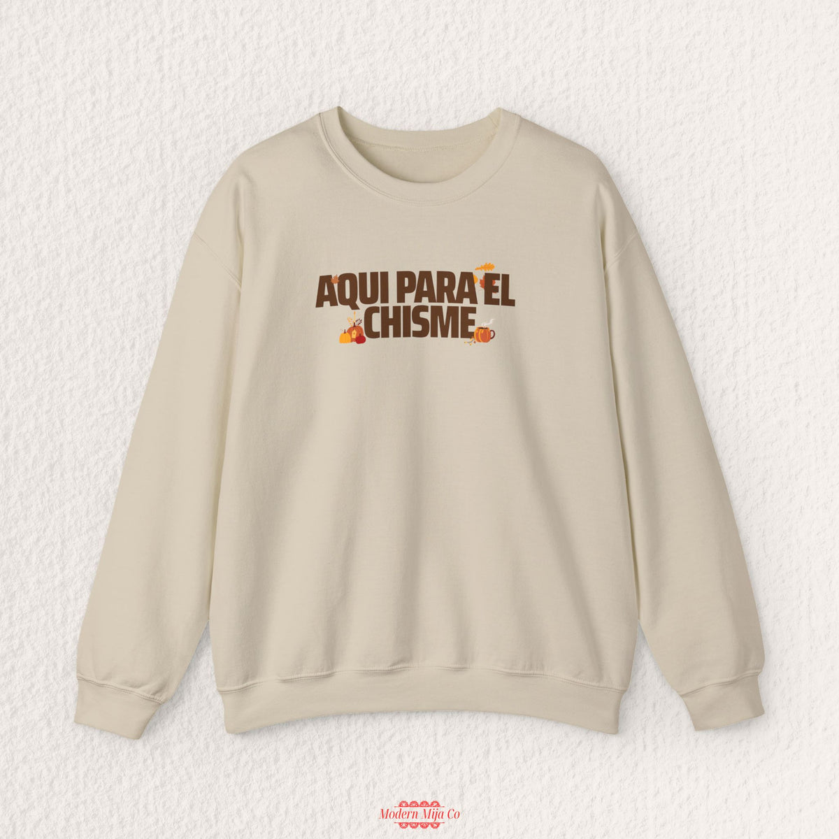 A beige crewneck sweatshirt with a brown and orange graphic text reading 'AQUI PARA EL CHISME' on the chest, displayed flat against a textured white background.