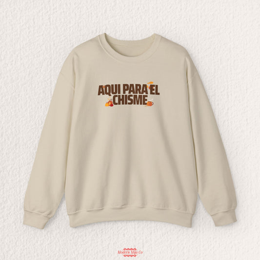A beige crewneck sweatshirt with a brown and orange graphic text reading 'AQUI PARA EL CHISME' on the chest, displayed flat against a textured white background.