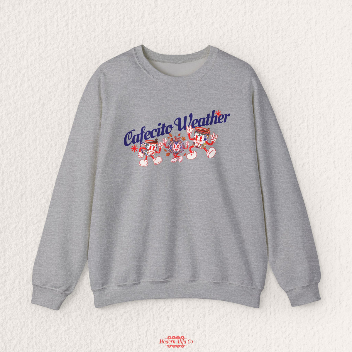 A heather gray crewneck sweatshirt featuring a 'Cafecito Weather' graphic with cartoon characters, displayed flat against a textured off-white background.