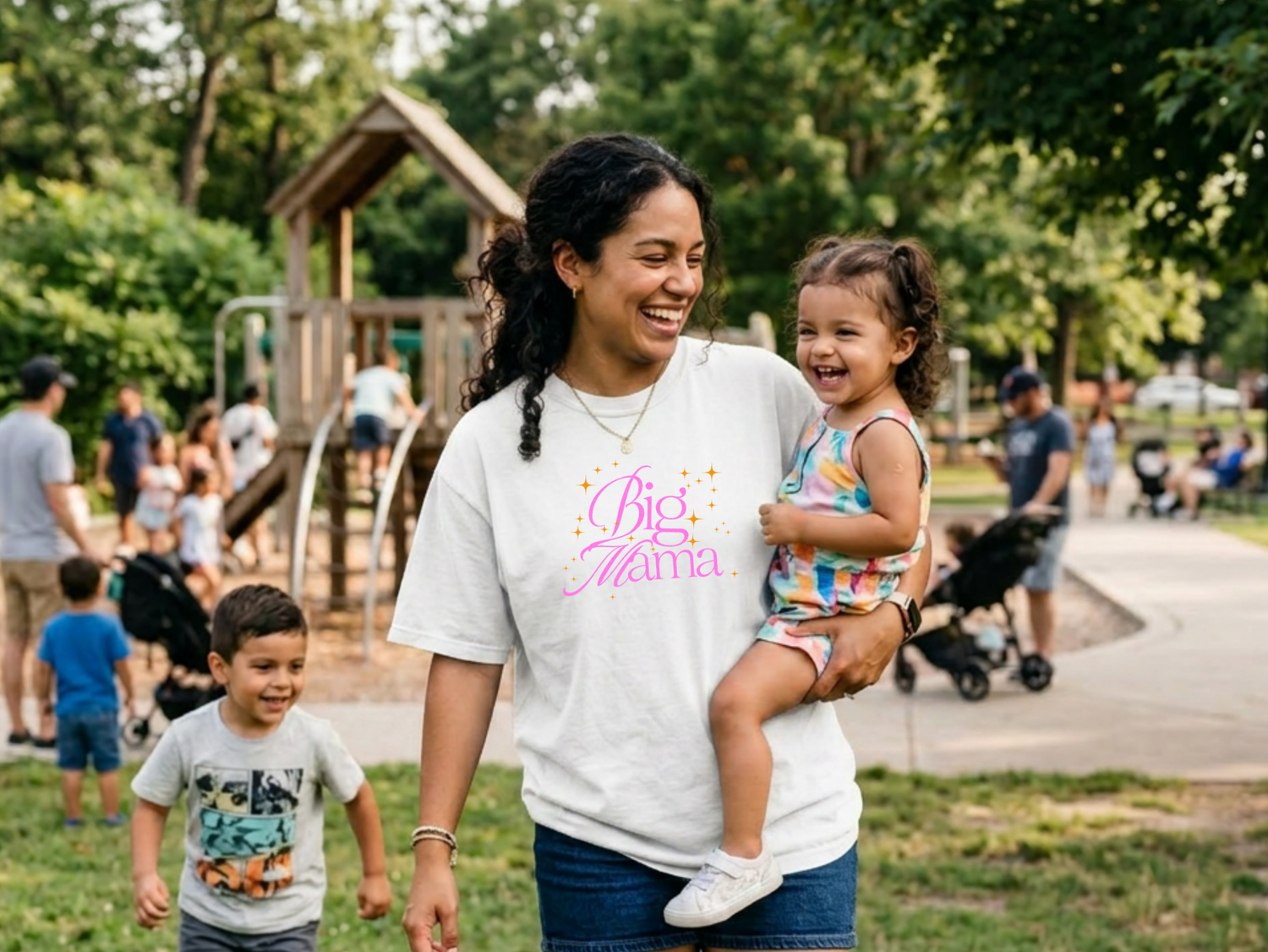 Woman holding a child in a park with playground equipment and other people in the background